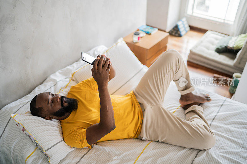 中年人躺在家里的床上玩智能手机