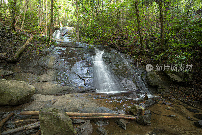 长曝光的流动的水在倾斜的瀑布面对原木在前景