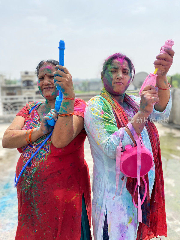 图片二，印度教的印度妇女站在油漆粉末的颜色，手持水枪，在胡里节的颜色和爱油漆和水战斗，看着相机