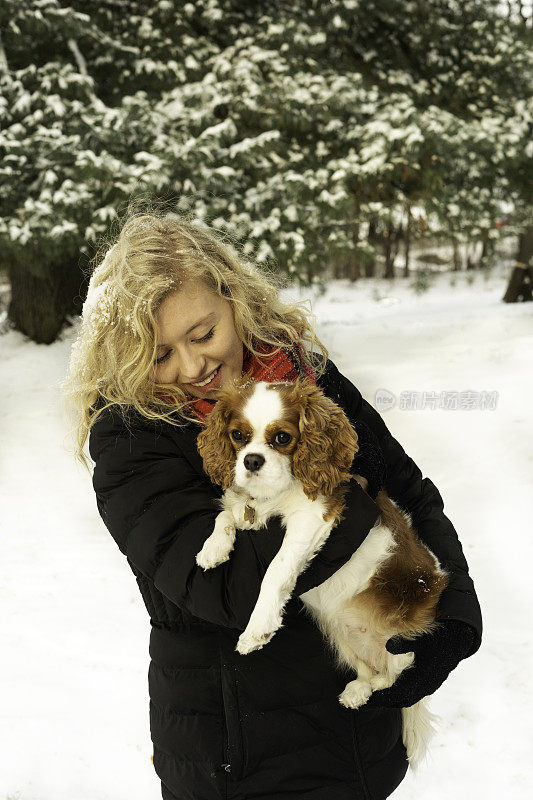 一位金发女子在雪地里抱着一只查理骑士猎犬