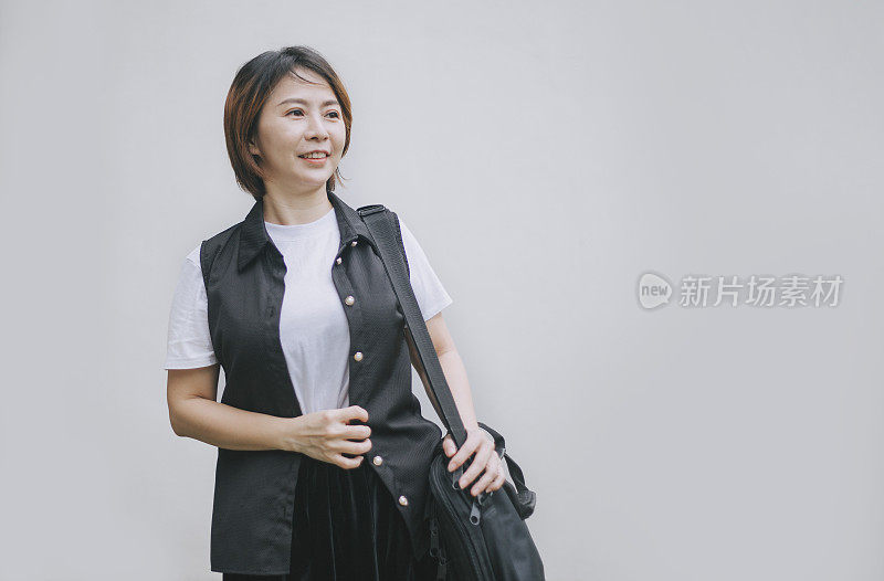 亚洲华人中年妇女带着笔记本电脑包走在白色背景下微笑
