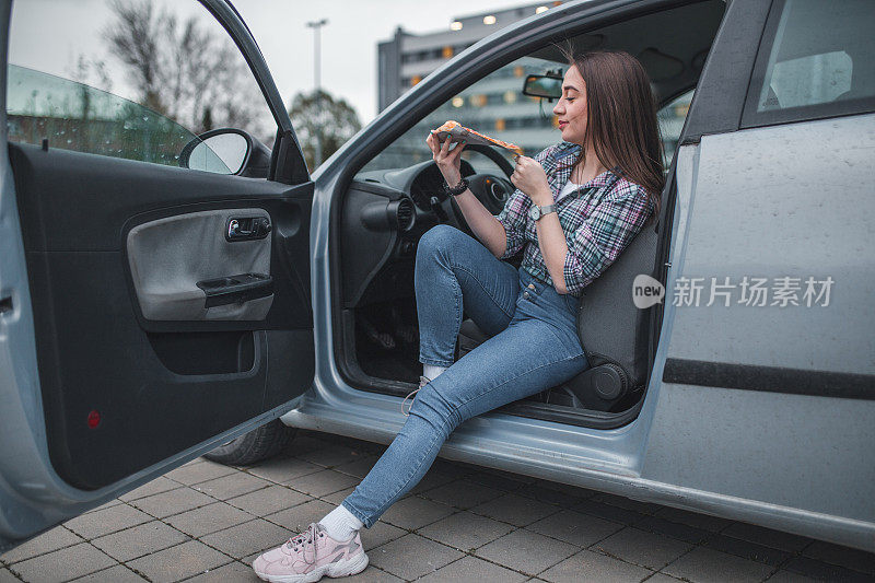 年轻的女司机在停车场吃披萨