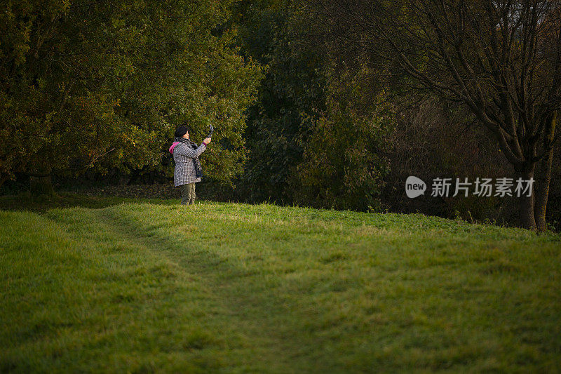 一位女士正在公园里拍摄秋天的日落