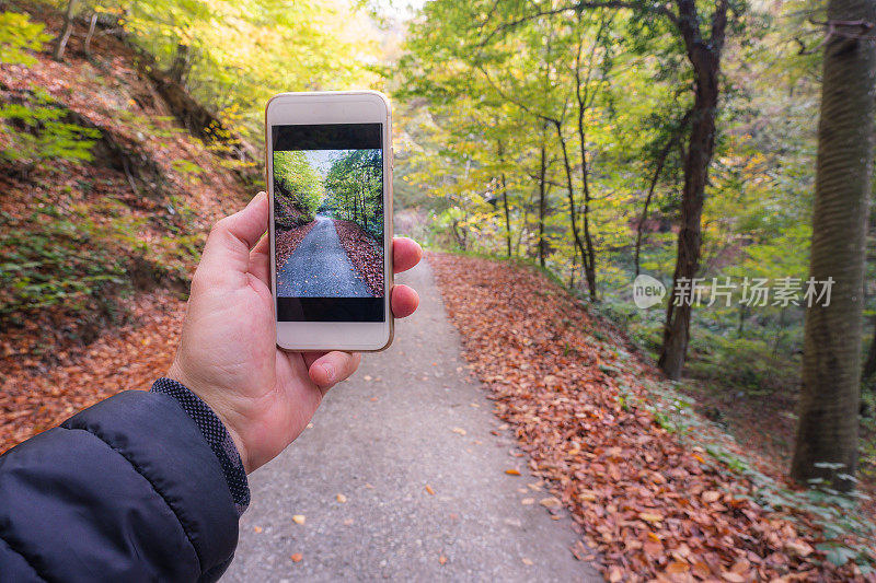 一名男子在秋天用智能手机远足时拍照
