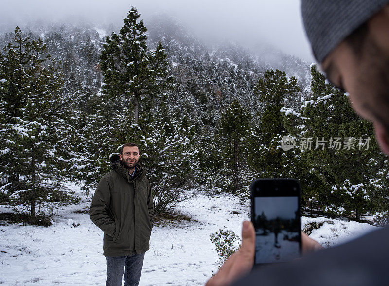 一名男子在雪景中用智能手机给朋友拍照