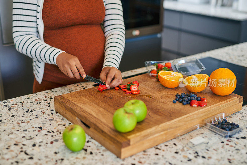 一个认不出来的孕妇在她的厨房里做水果沙拉
