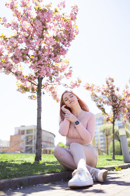 快乐时尚的年轻女子附近开花樱花树户外。春天看起来