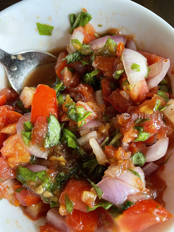 自制的番茄和洋葱沙拉的特写图像与罗勒叶混合在白色碗与金属勺子，提高的观点