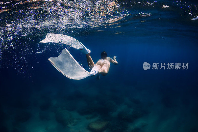 带着白色自由潜水脚蹼的女子在蓝色海洋的水面下游泳
