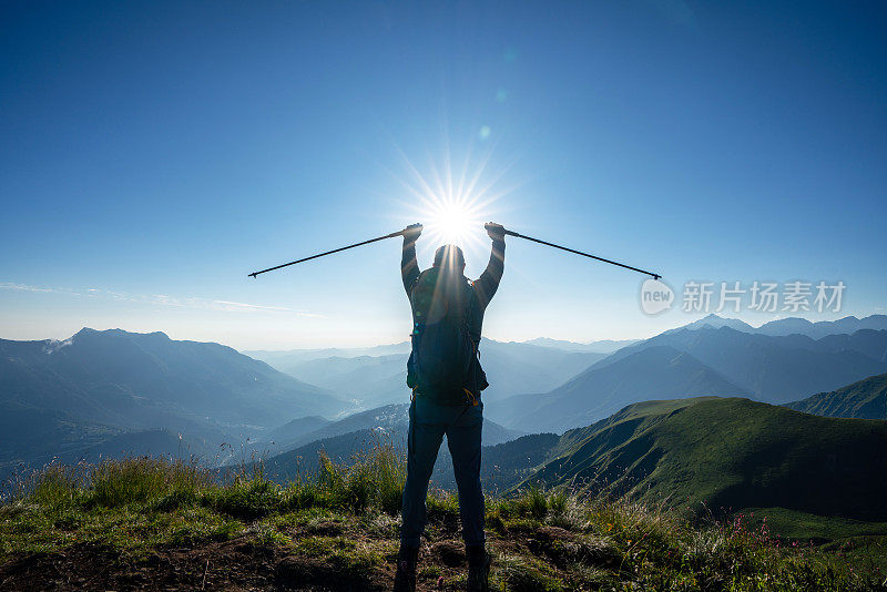 夕阳西下，山顶上徒步者的剪影高举着登山杖