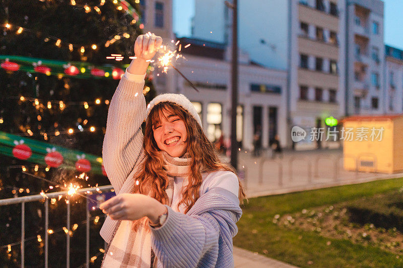 一名快乐的年轻女子在户外的一棵大圣诞树前手持烟火