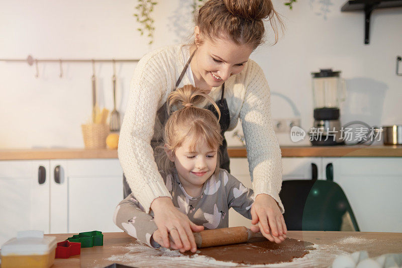 快乐的年轻妈妈和可爱的小女儿一起在家里的厨房里做手工饼干，擀面