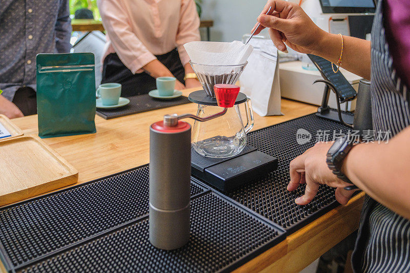咖啡师或咖啡店老板正在做一杯滴漏咖啡，而他的顾客正坐在咖啡馆的吧台前