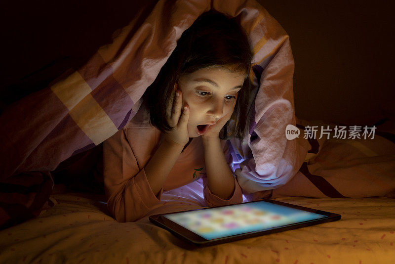 小女孩晚上在床上用平板电脑
