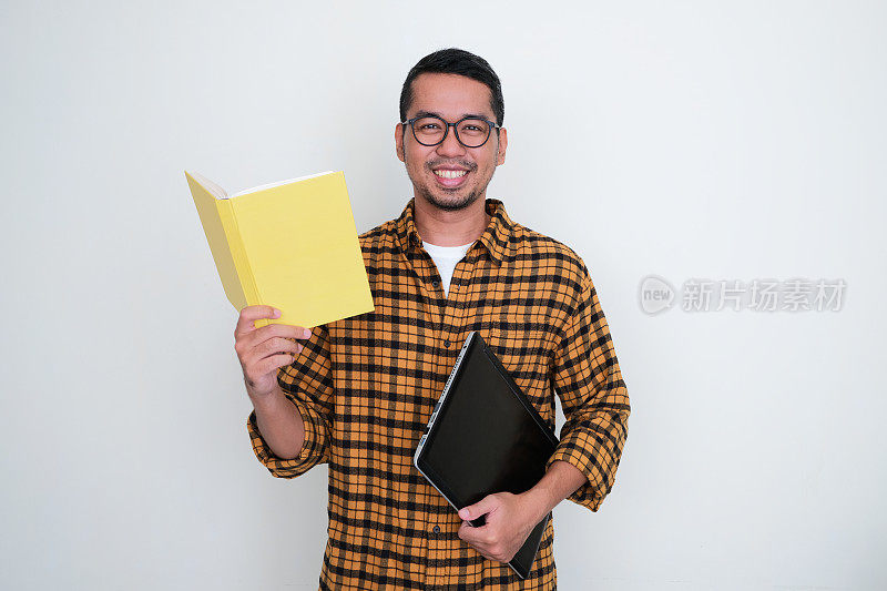 成年亚洲男子拿着笔记本电脑和书对着镜头微笑