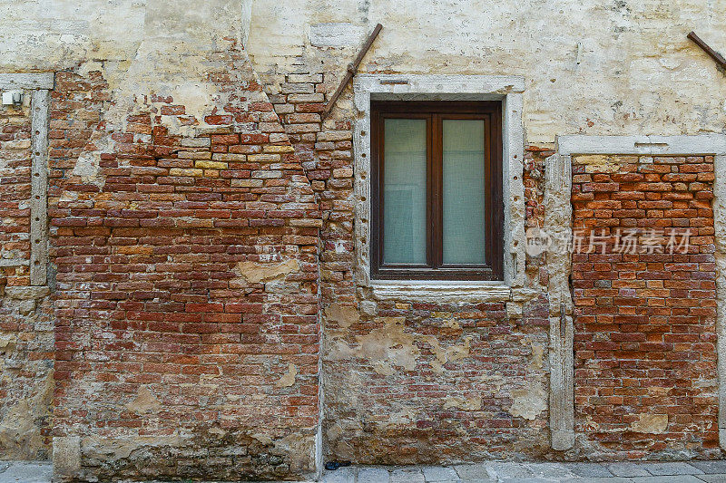 意大利威尼托威尼斯的一条小巷(“calle”)里，一座老砖房的细节，外面有一座壁炉，一扇没有百叶窗的窗户和一扇带墙的门