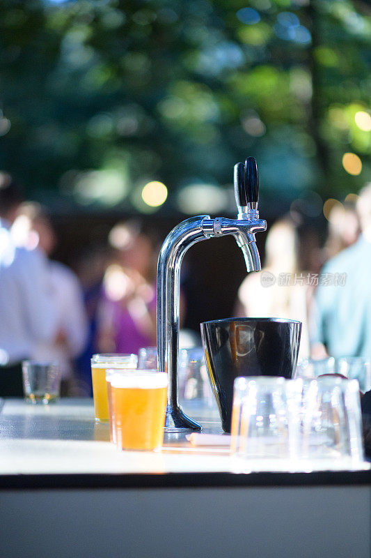 在一个阳光明媚的户外活动中，啤酒龙头和刚倒入玻璃杯的精酿啤酒