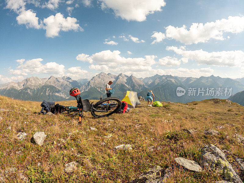 一对夫妇在瑞士阿尔卑斯山骑自行车，日落时分在山顶搭起帐篷