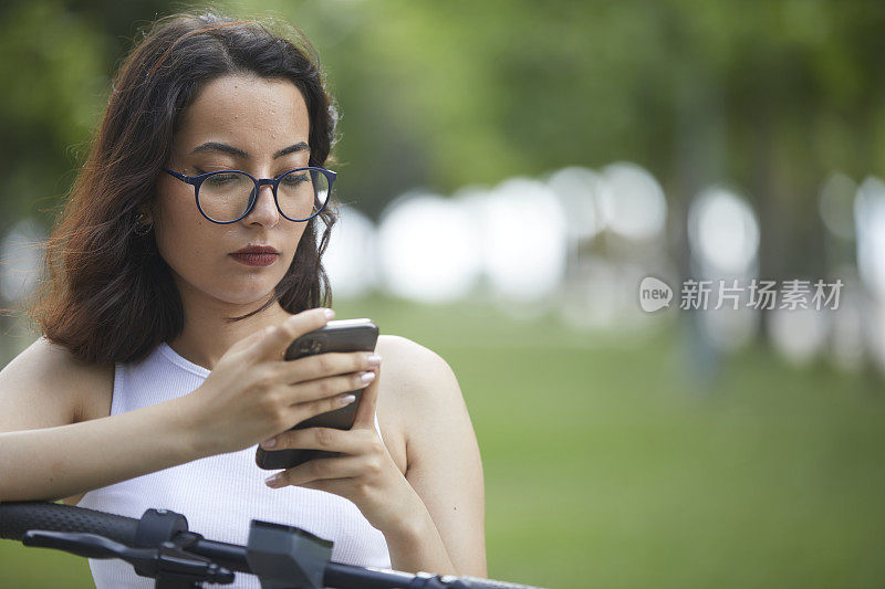 年轻的黑发女士一边玩电动滑板车一边看手机