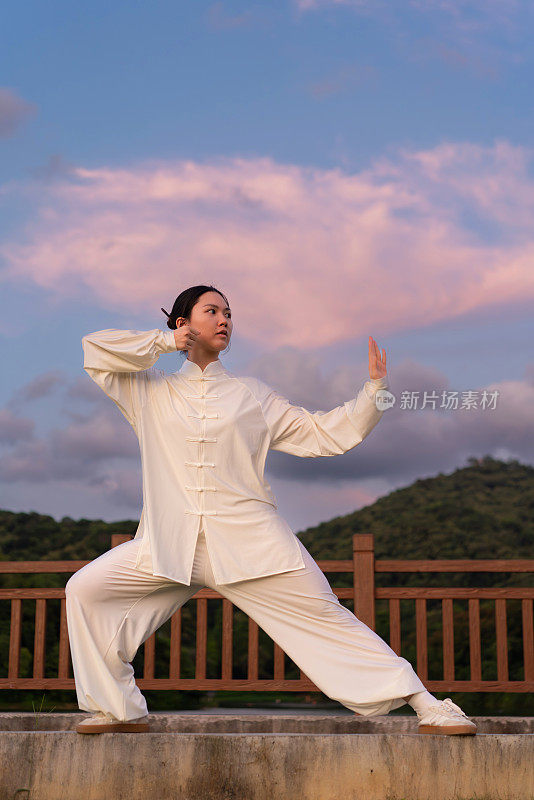 一位亚洲妇女正在公园里练习健身运动太极拳。