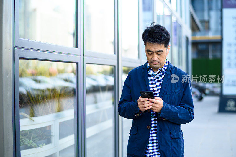 亚洲中年商人在城市街道上使用数码平板电脑