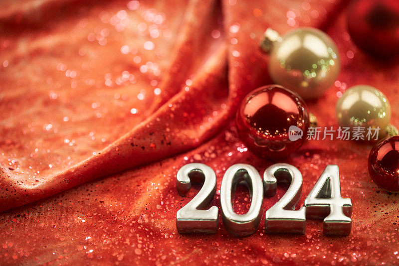 2024年新年快乐!闪亮的数字在红色的织物背景与圣诞装饰。