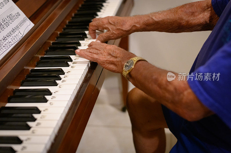 年长的成年男子双手若有所思地弹奏着一架立式钢琴