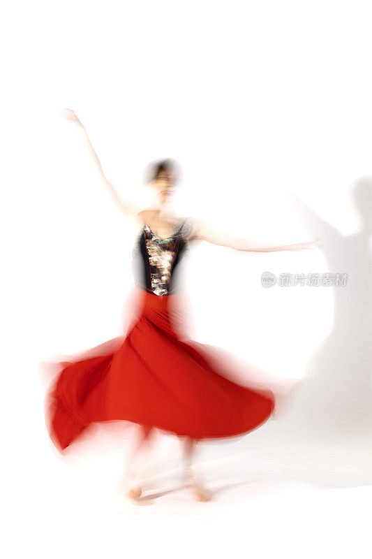 穿着红裙子的年轻芭蕾舞女演员在舞蹈室的灯光下跳舞。长时间的曝光。白色背景