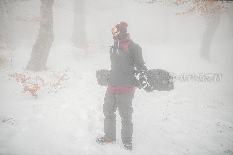 在一个雾蒙蒙的冬日，一名男子准备骑滑雪板