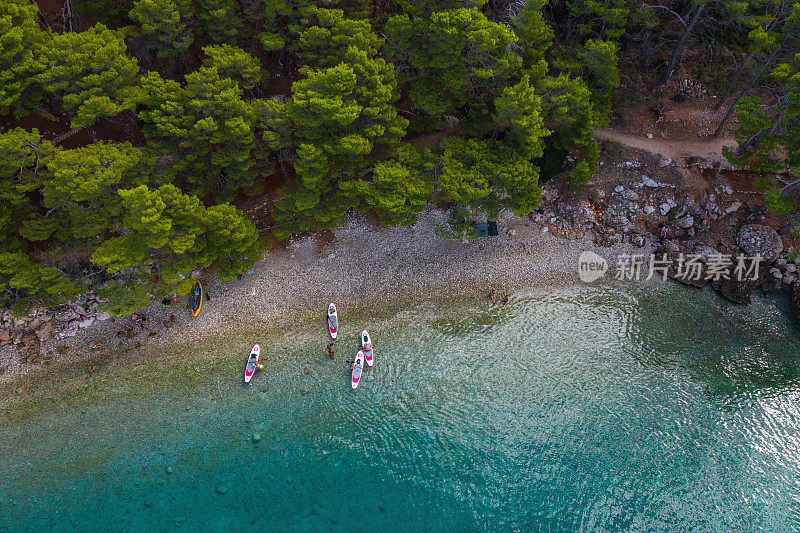无人机航拍图。美丽的海岸线。岸边长满了松树。游客骑在游泳板上，俯视图。克罗地亚。Makarska里维埃拉