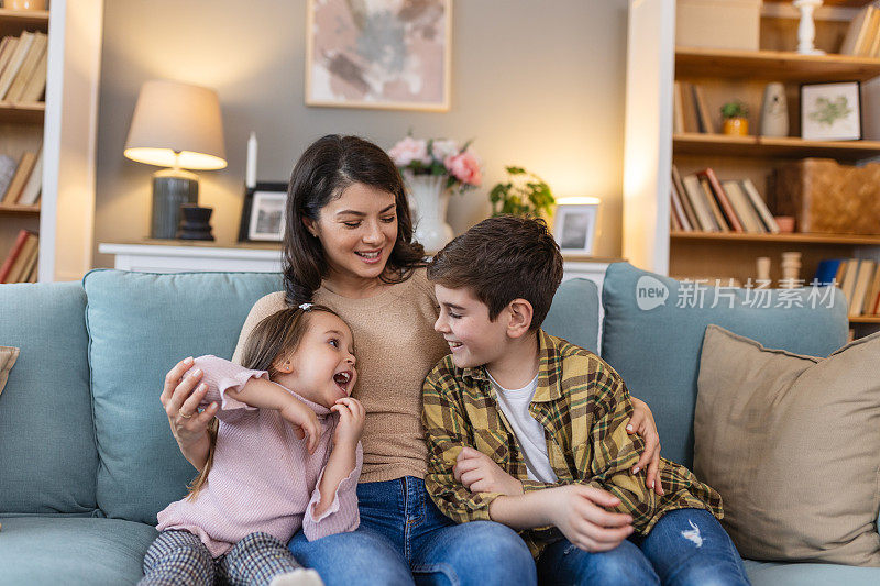 在熟悉舒适的客厅里，一位母亲、她的女儿和她的儿子围坐在沙发上，他们创造了一个充满爱和联系的场景，分享笑声和家庭生活的故事。