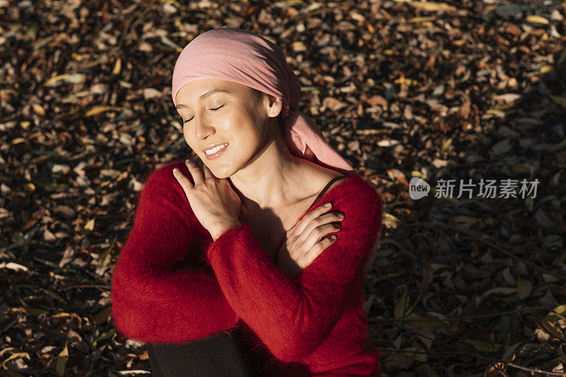 一位癌症患者坐在那里拥抱自己，微笑着享受阳光