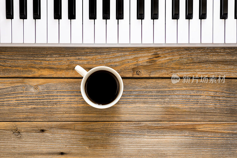 木制背景上的钢琴键和一杯咖啡，俯视图。
