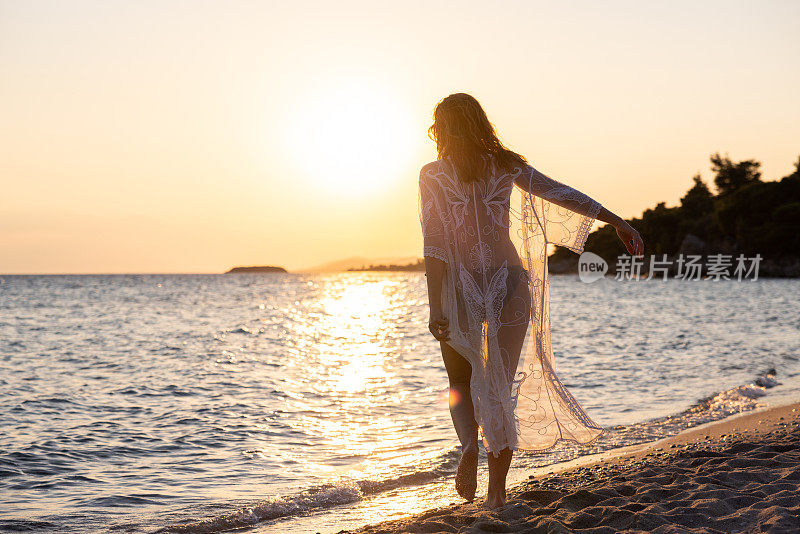 难以辨认的年轻女子在海滩上欣赏日落