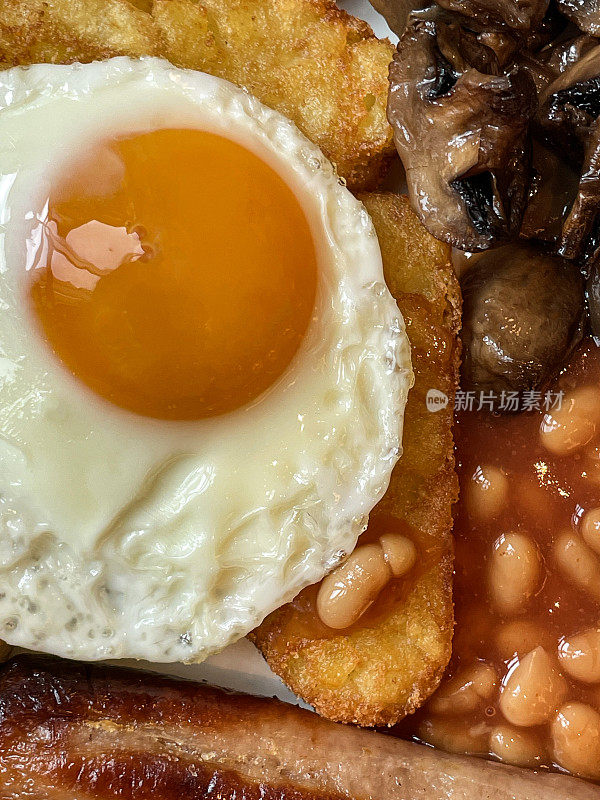 全英式油炸早餐食材，一堆烤豆，单面煎蛋，一堆蘑菇，香肠和两个土豆饼，高架视图