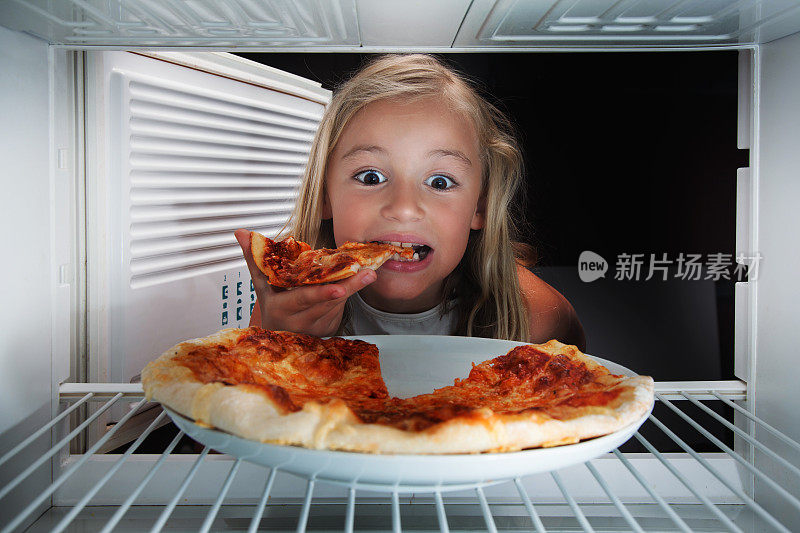 饥饿的女孩正在吃冰箱里的披萨