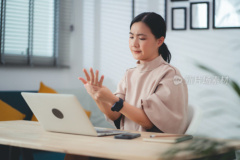 一名亚洲女性在家办公时患手痛。