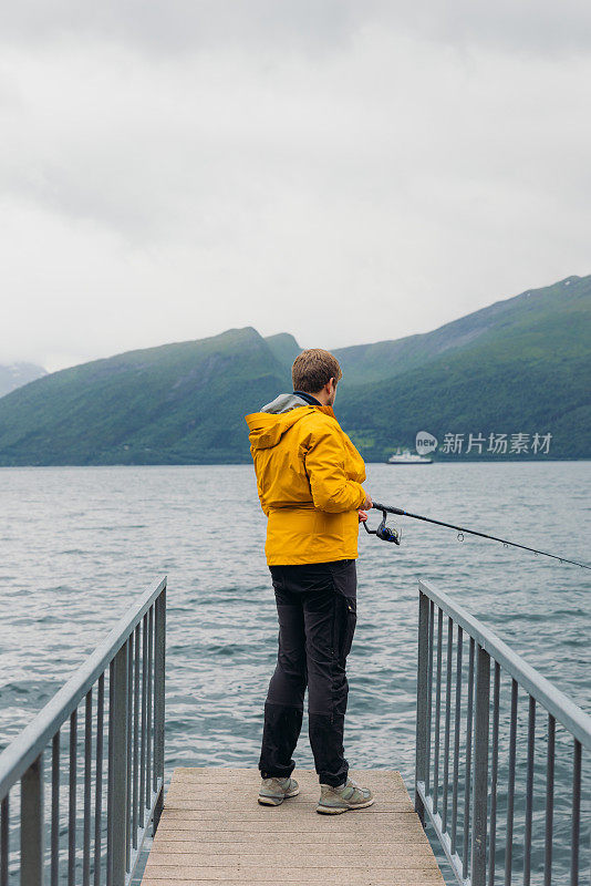 身穿黄夹克的男子在挪威峡湾边钓鱼