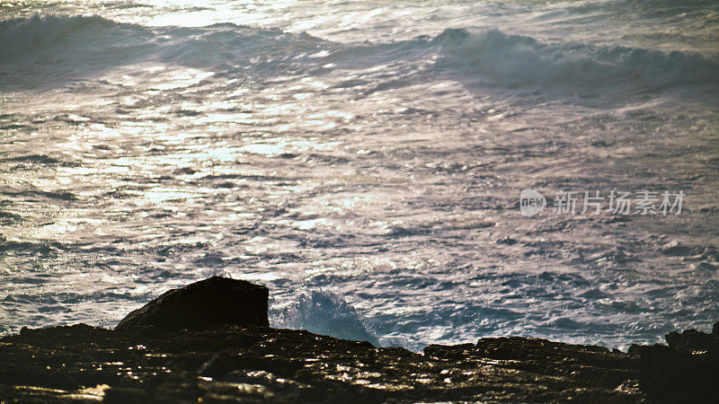 清晨，浅浅的海浪拍打着岩石。波光粼粼的水面反射