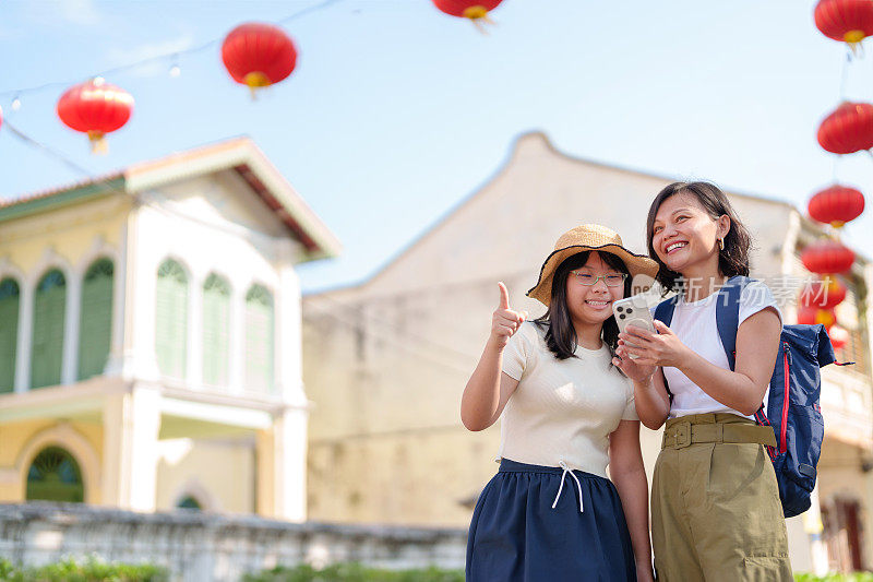 一对快乐的母女在槟城乔治城的街道上探索，用智能手机来提升他们的旅行体验。