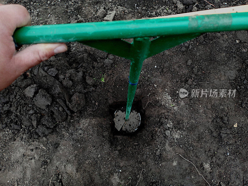 在地面上钻一口井，借助手工绿钻自己动手。用钻孔法挖洞。地面上的绿色钻头在土壤上钻了一个洞。
