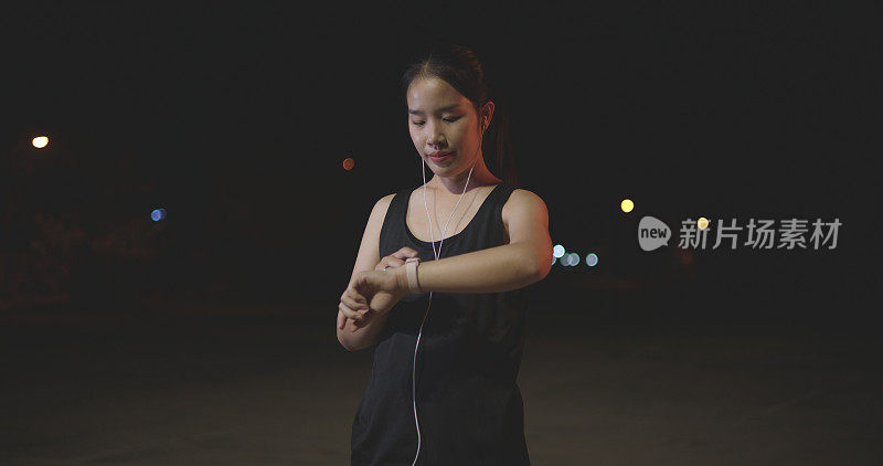年轻的女运动员使用智能手表跟踪健身目标，并在晚上训练前热身时检查心率。