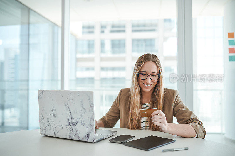 快乐的女商人拿着信用卡，在办公室用笔记本电脑网购