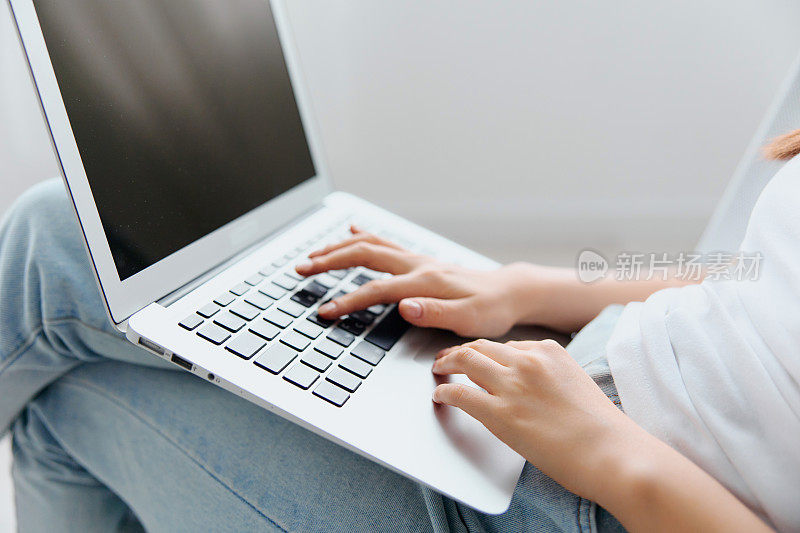 在室内客厅里，可爱的年轻亚洲女性用笔记本电脑输入信息加载NFT项目。远程通信远程工作社交媒体概念。很酷的横幅模型