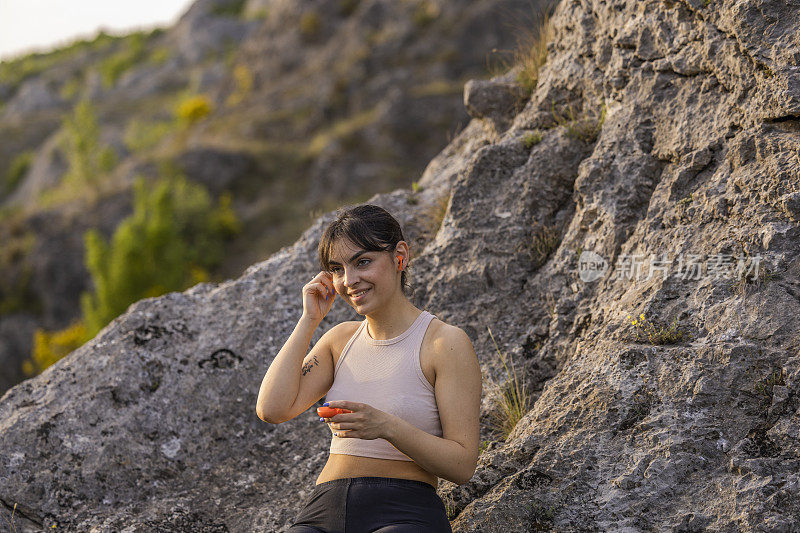 女孩戴着无线耳机，如何在户外训练成功后，坐在岩石上享受良好的氛围和新鲜的空气。