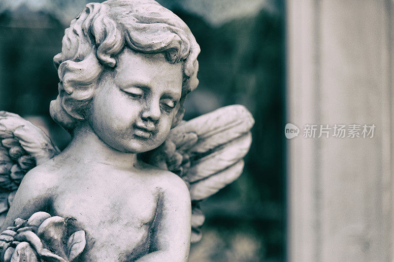 美丽的丘比特雕像的天使在复古花园在夏天。手里拿着一束花