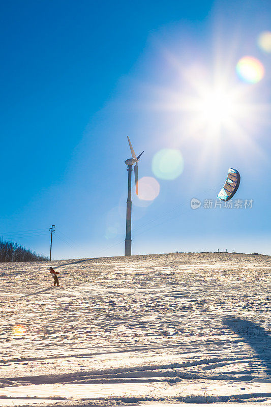在风力涡轮机下和冬日的阳光下玩雪