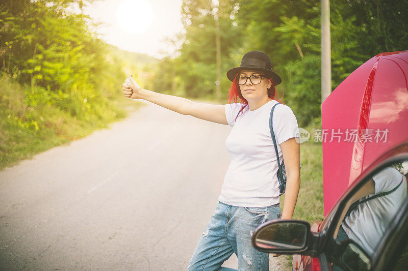 带着帽子和背包的女孩在路上搭便车