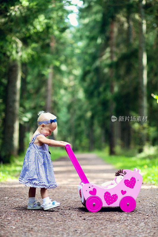 漂亮的小女孩推着她的娃娃婴儿车