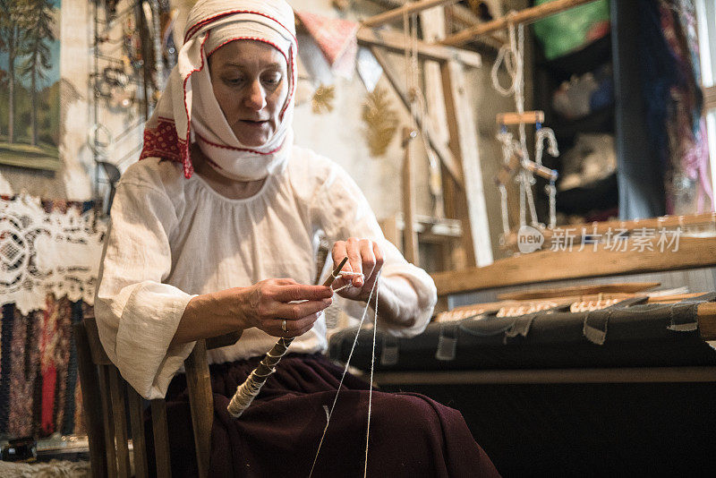 成熟的白俄罗斯妇女穿着传统服装在老式织布机旁纺纱